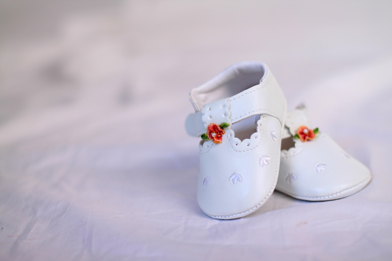 Babyschuhe in weiß mit roten Blümchen stehen auf einem weißen Tuch - Taufschuhe?